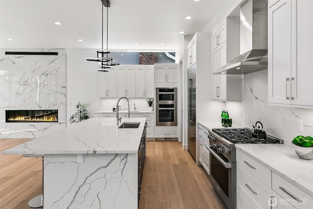 kitchen featuring stainless steel appliances, decorative backsplash, a high end fireplace, a sink, and wall chimney exhaust hood