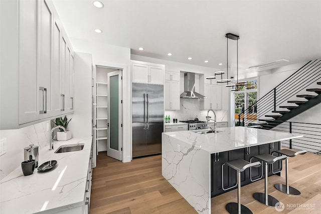 kitchen featuring light wood finished floors, wall chimney exhaust hood, appliances with stainless steel finishes, and a sink