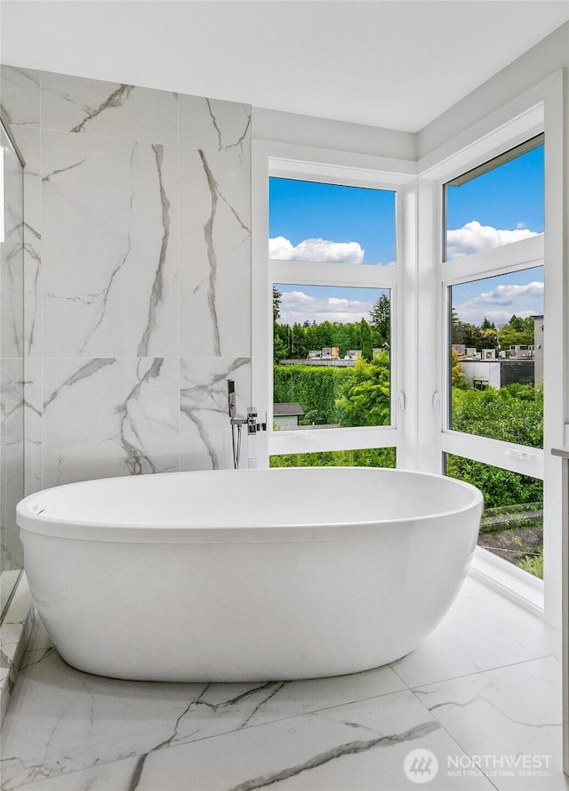 bathroom with stone wall, marble finish floor, and a freestanding tub