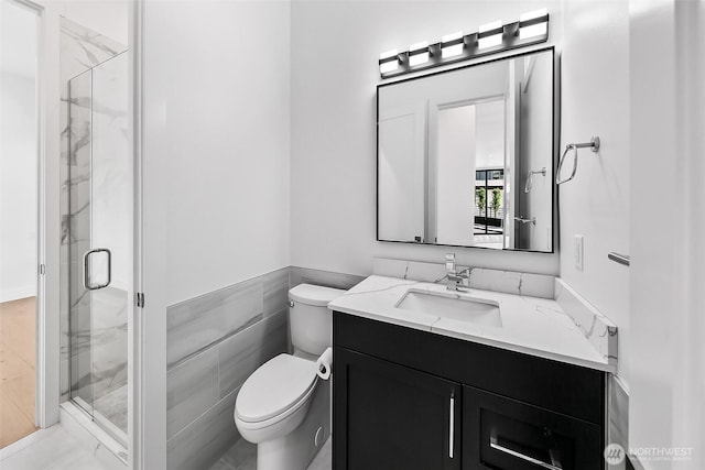 bathroom with toilet, a marble finish shower, tile walls, and vanity