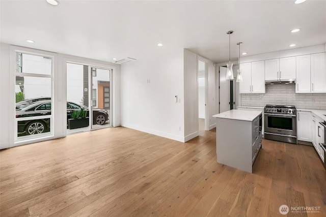 kitchen with under cabinet range hood, light wood-style floors, light countertops, high end stainless steel range, and decorative backsplash