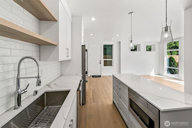 kitchen with backsplash, light wood-style flooring, gray cabinetry, appliances with stainless steel finishes, and a sink