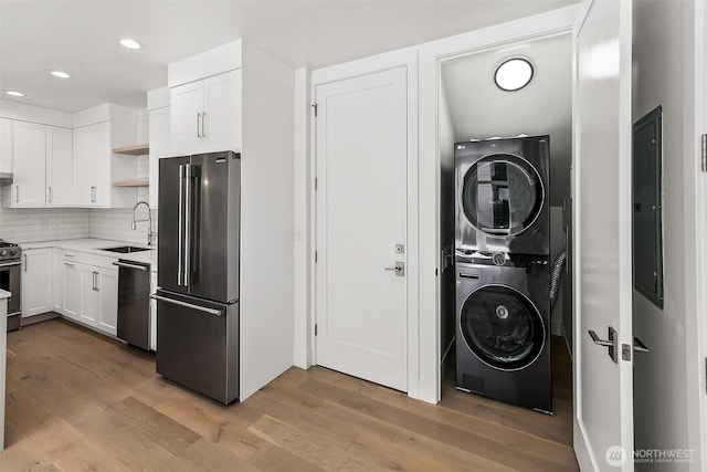 kitchen with stainless steel appliances, wood finished floors, a sink, stacked washing maching and dryer, and open shelves