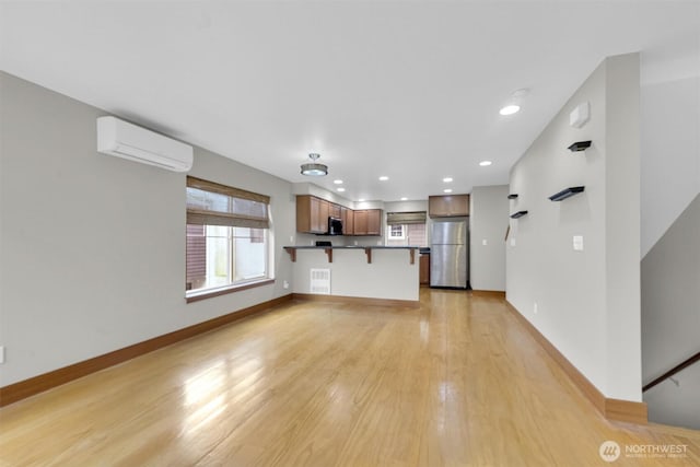 unfurnished living room featuring recessed lighting, visible vents, baseboards, an AC wall unit, and light wood-type flooring