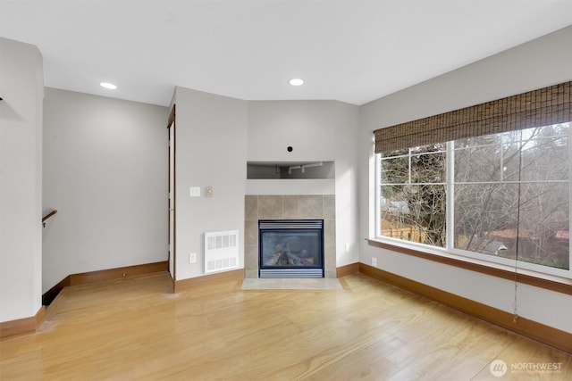 unfurnished living room with recessed lighting, visible vents, a tiled fireplace, light wood-type flooring, and baseboards