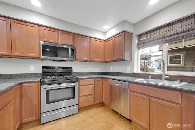 kitchen featuring dark countertops, stainless steel appliances, light wood-type flooring, a sink, and recessed lighting