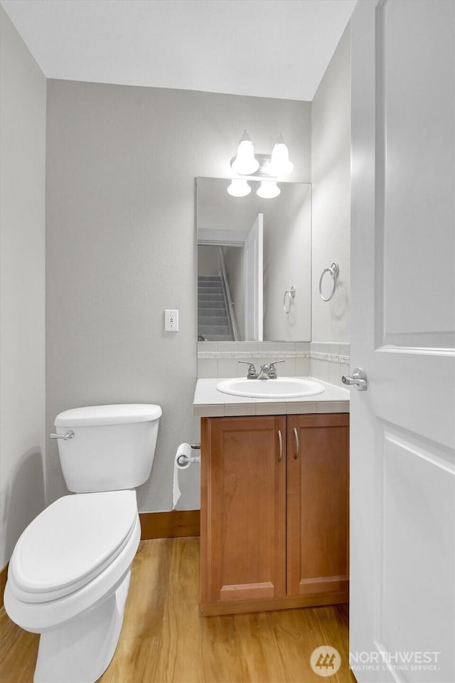 half bathroom with wood finished floors, vanity, toilet, and baseboards