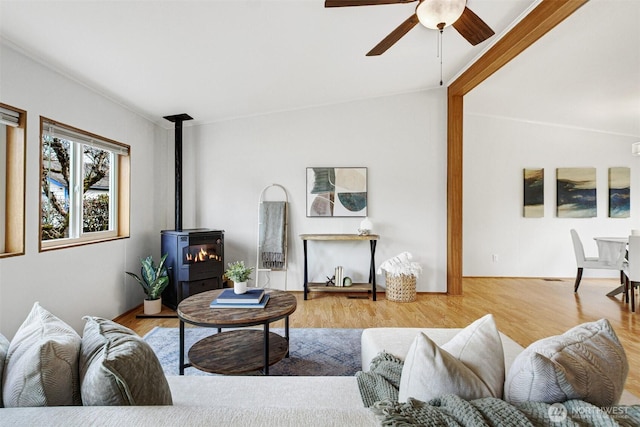 living area with ceiling fan, wood finished floors, and a wood stove