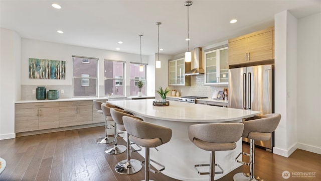 kitchen featuring high end fridge, wall chimney range hood, range, dark wood-style floors, and a kitchen bar