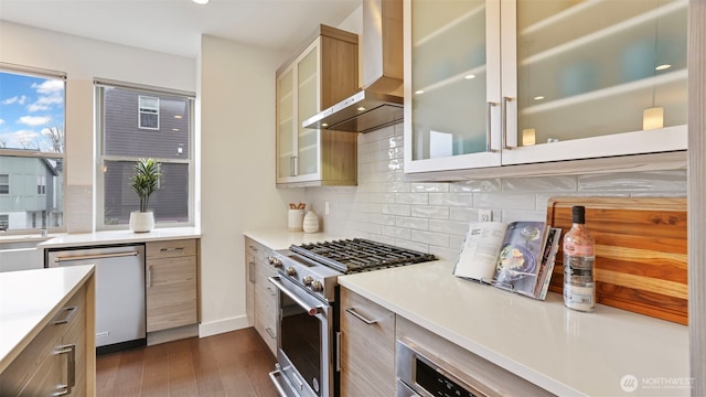 kitchen featuring dark wood-style flooring, stainless steel appliances, tasteful backsplash, light countertops, and wall chimney range hood