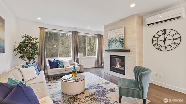 living room featuring an AC wall unit, a tiled fireplace, wood finished floors, and baseboards