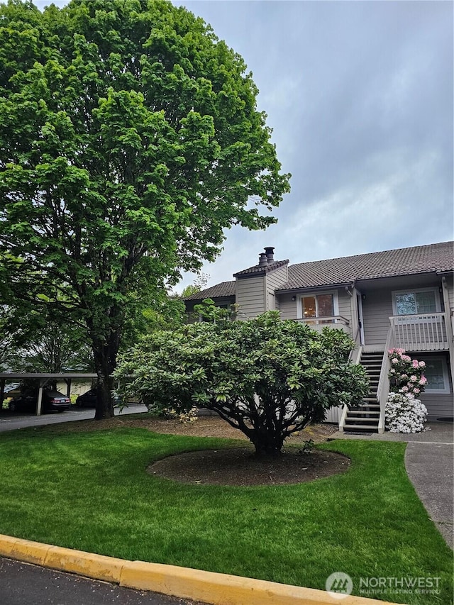 view of front of property featuring a front yard, a chimney, a tile roof, and stairway