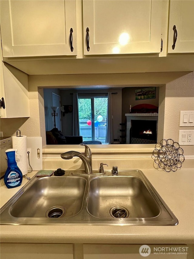 room details featuring a warm lit fireplace, white cabinets, a sink, and light countertops