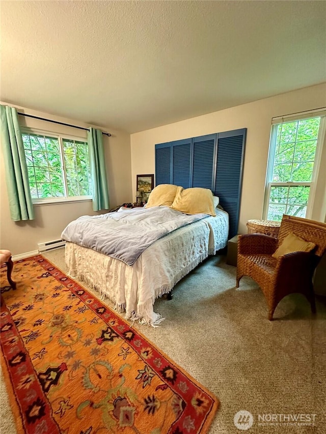 bedroom with carpet floors, multiple windows, a baseboard heating unit, and a textured ceiling