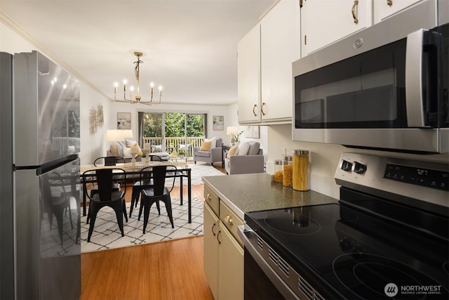 kitchen with open floor plan, white cabinetry, stainless steel appliances, an inviting chandelier, and light wood finished floors