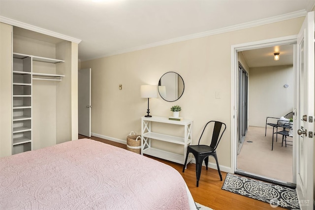 bedroom with a closet, crown molding, baseboards, and wood finished floors