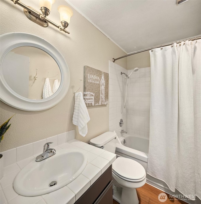 bathroom featuring toilet, shower / bath combo with shower curtain, wood finished floors, a textured wall, and vanity