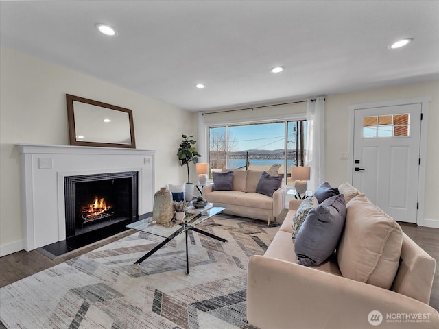 living room featuring recessed lighting, a lit fireplace, baseboards, and wood finished floors