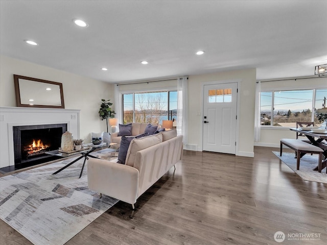 living area featuring dark wood-style floors, a warm lit fireplace, baseboards, and recessed lighting