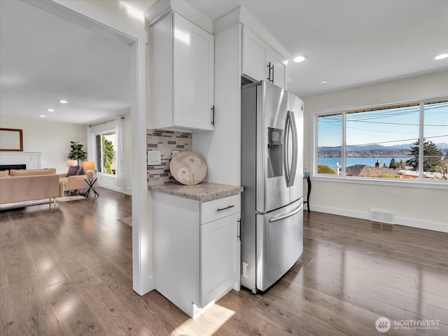 kitchen with visible vents, white cabinets, wood finished floors, stainless steel refrigerator with ice dispenser, and backsplash