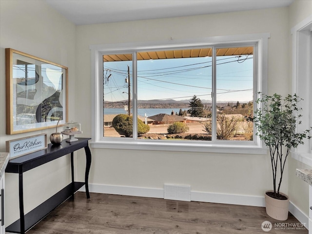 sitting room with visible vents, dark wood finished floors, baseboards, and a water view