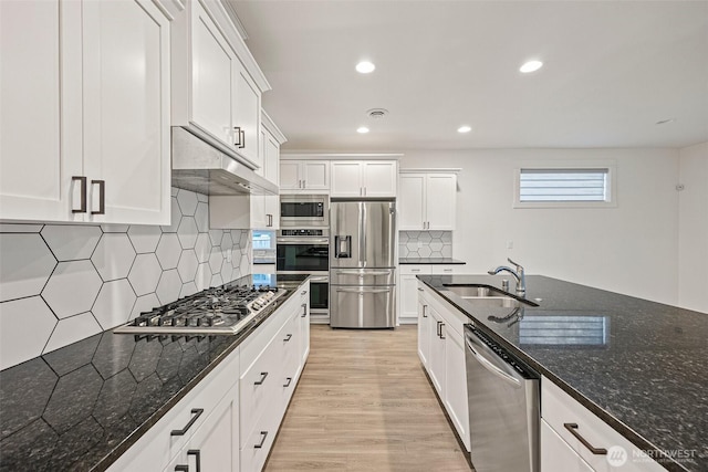 kitchen featuring light wood finished floors, white cabinets, stainless steel appliances, under cabinet range hood, and a sink