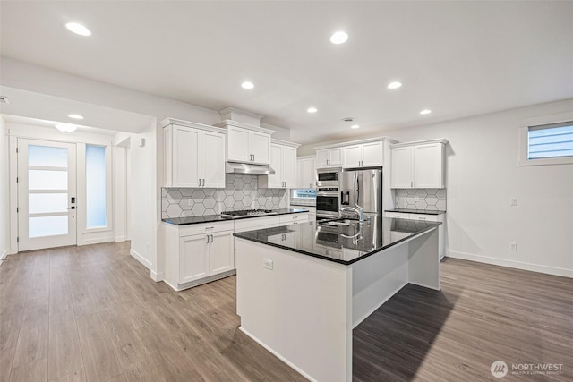 kitchen with dark countertops, under cabinet range hood, stainless steel appliances, and light wood finished floors