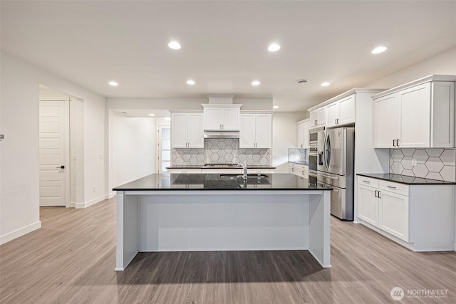 kitchen featuring light wood-style flooring, under cabinet range hood, a sink, appliances with stainless steel finishes, and dark countertops