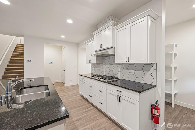 kitchen with light wood-style flooring, stainless steel gas stovetop, a sink, and under cabinet range hood