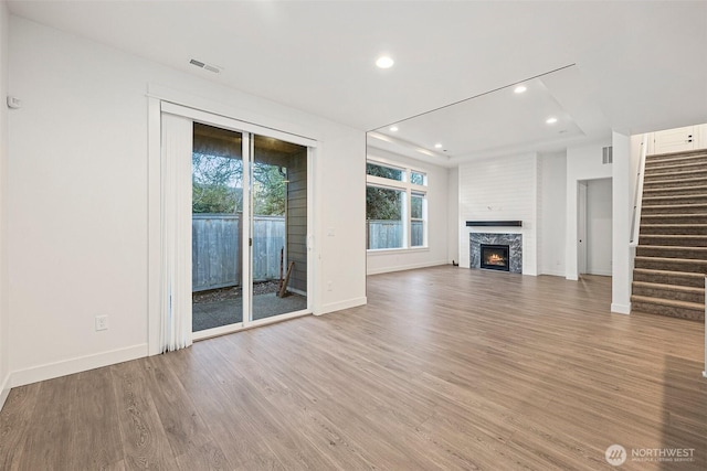 unfurnished living room with a warm lit fireplace, baseboards, light wood-style flooring, stairway, and recessed lighting