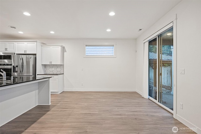 kitchen featuring decorative backsplash, dark countertops, stainless steel appliances, light wood-type flooring, and white cabinetry