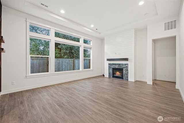 unfurnished living room with a tray ceiling, wood finished floors, and visible vents