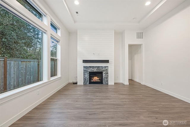 unfurnished living room featuring a tray ceiling, wood finished floors, visible vents, and baseboards