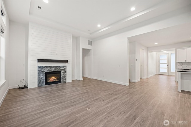 unfurnished living room featuring a tray ceiling, a fireplace, light wood finished floors, visible vents, and baseboards