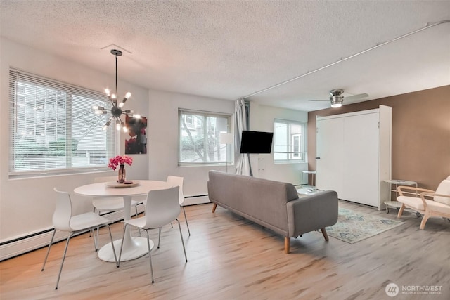 living area featuring a textured ceiling, ceiling fan with notable chandelier, wood finished floors, and a baseboard radiator