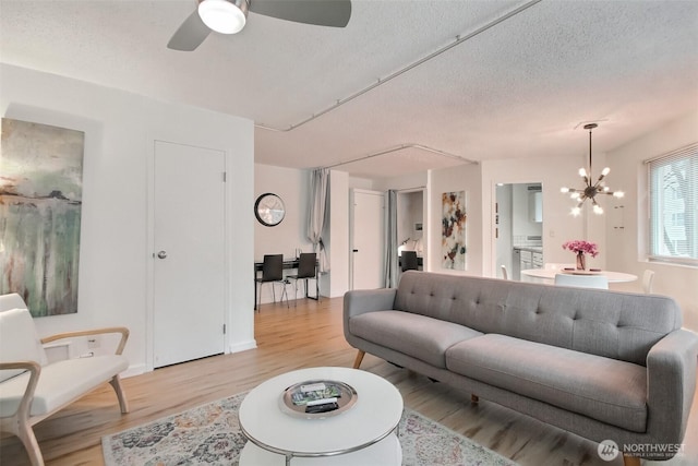 living room featuring light wood-style flooring, ceiling fan with notable chandelier, and a textured ceiling