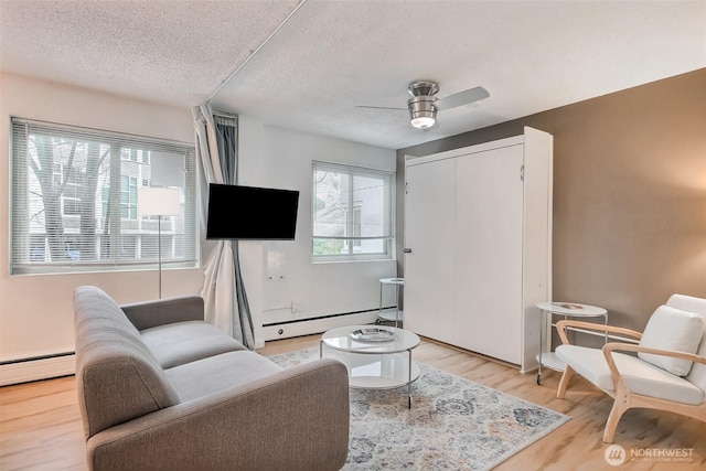 living area featuring ceiling fan, a baseboard heating unit, a textured ceiling, and light wood-style flooring