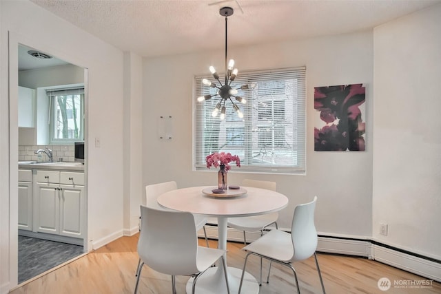 dining area featuring an inviting chandelier, light wood-style floors, baseboards, and a textured ceiling