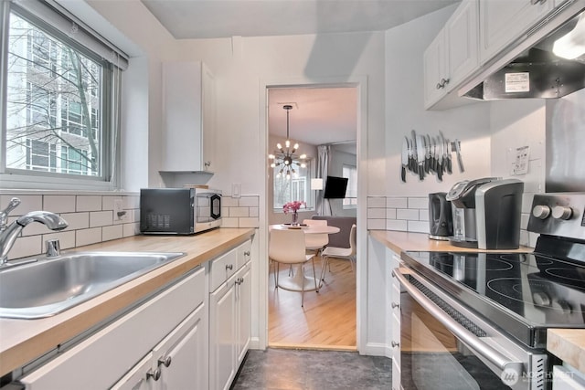 kitchen with under cabinet range hood, a sink, stainless steel appliances, white cabinets, and decorative backsplash