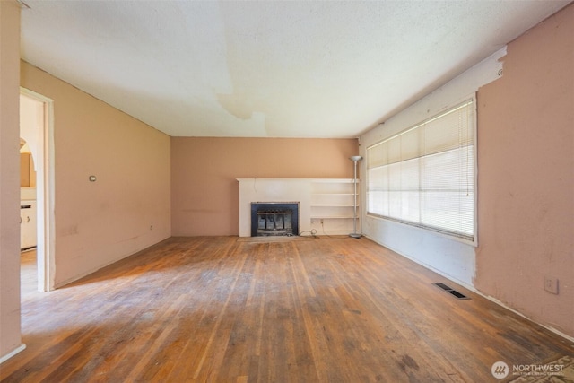 unfurnished living room with visible vents, a glass covered fireplace, and hardwood / wood-style flooring