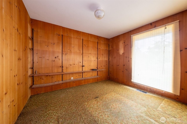 empty room with visible vents, carpet floors, and wood walls