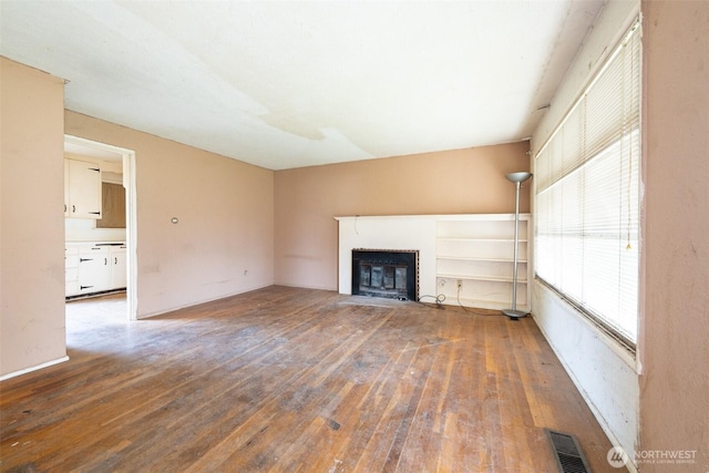 unfurnished living room with visible vents, wood-type flooring, and a fireplace with flush hearth