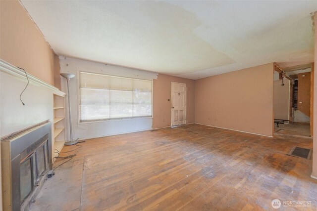 unfurnished living room with a glass covered fireplace, visible vents, and hardwood / wood-style floors