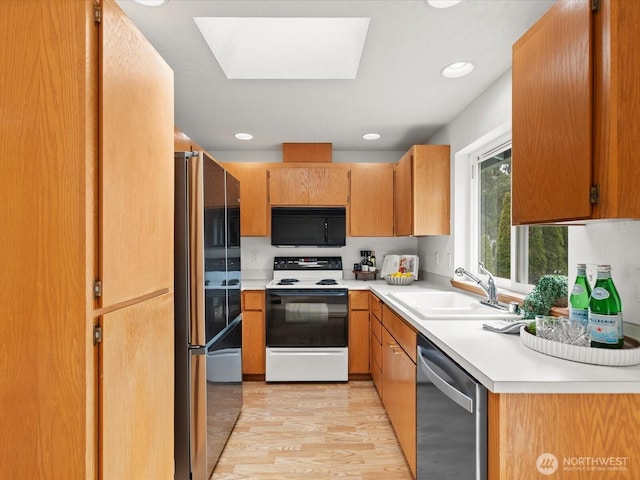 kitchen with light wood finished floors, a skylight, a sink, stainless steel appliances, and light countertops