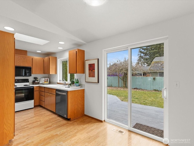 kitchen featuring range with electric cooktop, a sink, black microwave, light countertops, and dishwasher