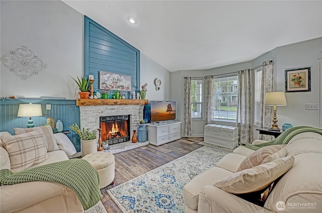 living area featuring a wainscoted wall, wood finished floors, a fireplace, and vaulted ceiling