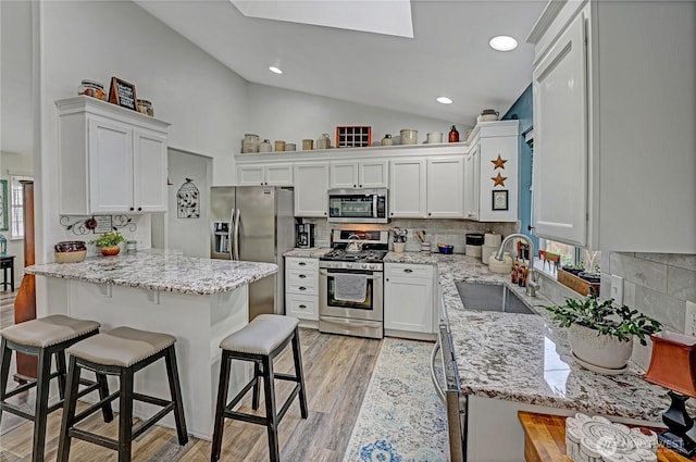 kitchen featuring a breakfast bar, vaulted ceiling with skylight, appliances with stainless steel finishes, white cabinets, and a sink