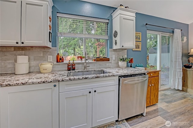 kitchen with tasteful backsplash, light wood-type flooring, stainless steel dishwasher, white cabinets, and a sink