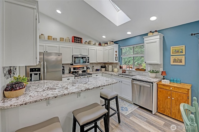 kitchen with a breakfast bar, a peninsula, a sink, appliances with stainless steel finishes, and backsplash