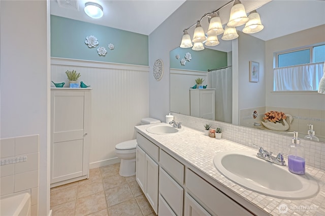 full bathroom with double vanity, visible vents, a wainscoted wall, and a sink